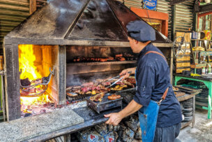 Chef grilling meats on an open flame Argentine-style barbecue.