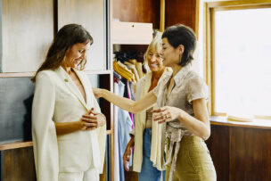 Three women stand in a clothing store in Buenos Aires, with one wearing a white suit while another adjusts it and the third woman smiles nearby—capturing one of the chic things to do while visiting Argentina.