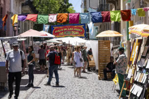 People walk through a colorful outdoor market on a cobblestone street in Buenos Aires, Argentina, with booths, umbrellas, and a banner reading "Feria de las Artes San Pedro Telmo"—one of the top things to do in the city.