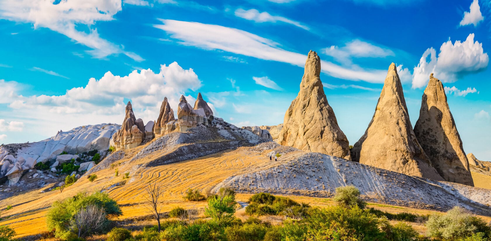 Rock formations and sparse vegetation under a blue sky with clouds in Cappadocia, Turkey—a breathtaking landscape that showcases why many consider this region the best time to visit Turkey.
