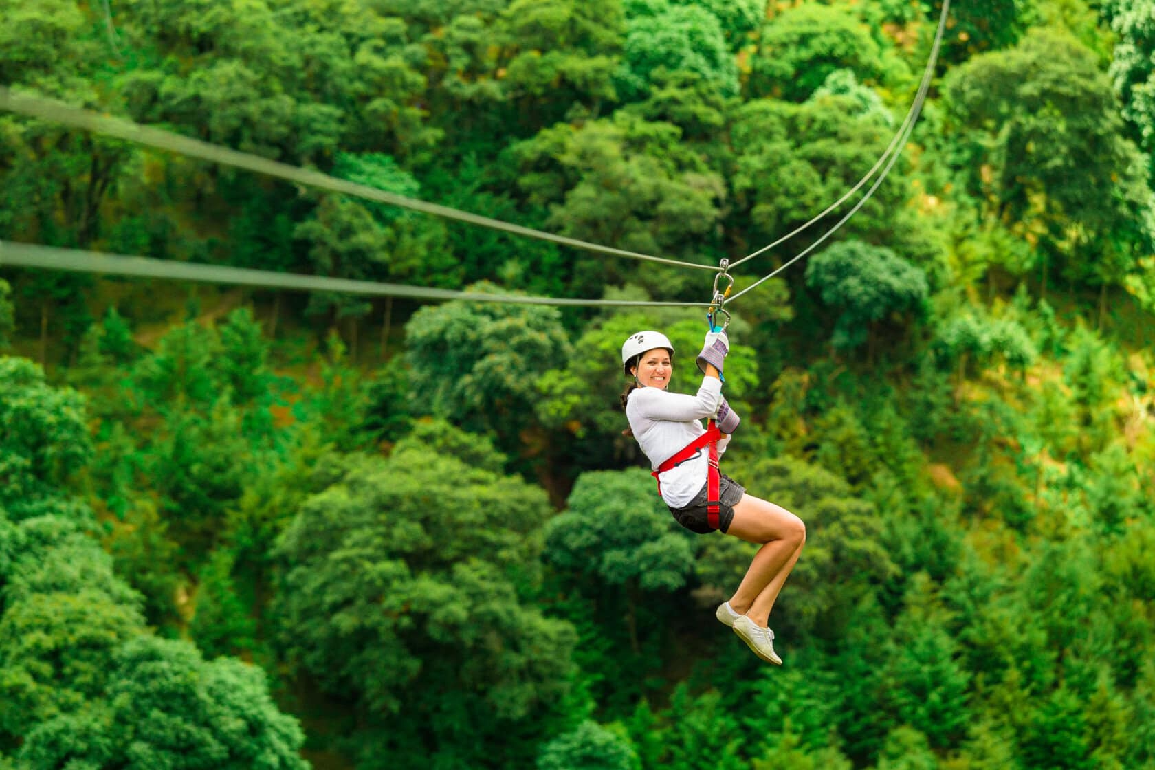 A person wearing a helmet and harness rides a zip line over a lush green forest in Costa Rica, smiling with legs bent—a thrilling adventure and one of the top things to do for travel enthusiasts.
