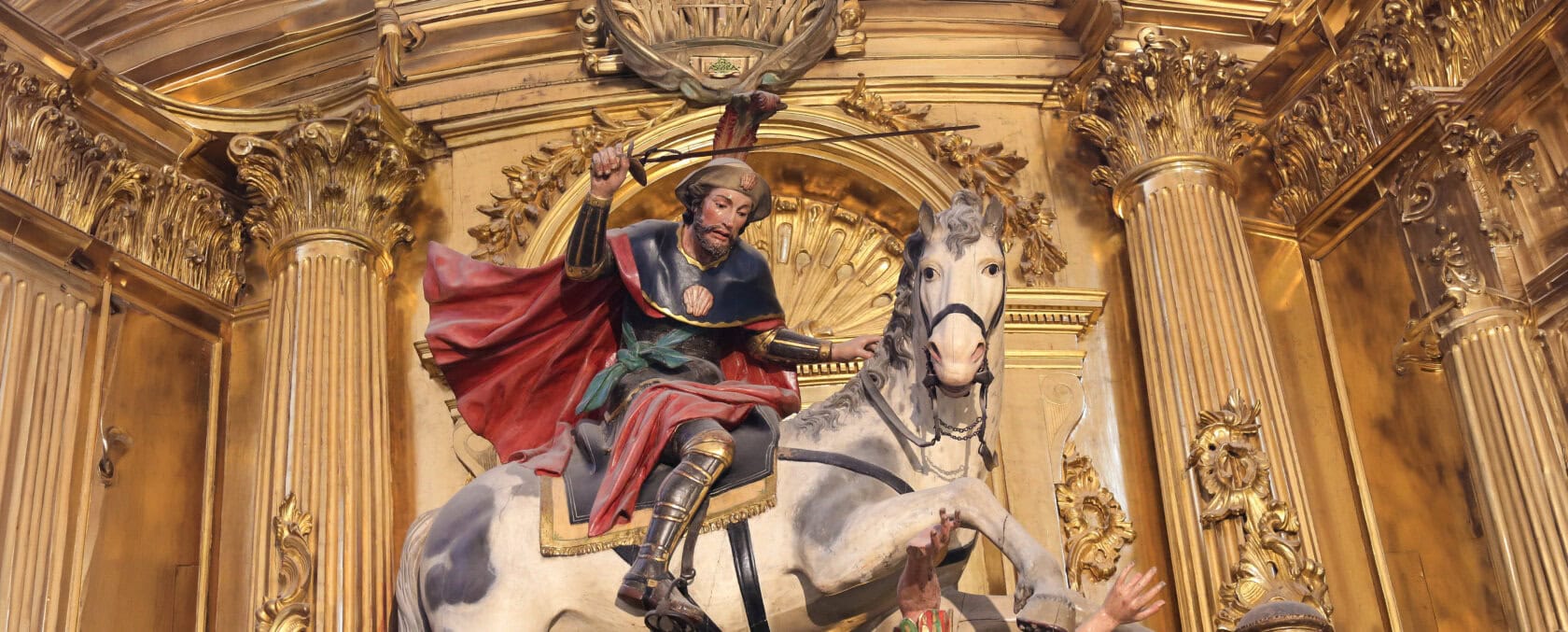Statue of a man in armor on a white horse holding a sword, set against an ornate gold background—evoking the rich history of pilgrimage along the Camino de Santiago.