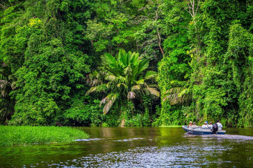 A small boat with people moves along a river bordered by dense green tropical rainforest vegetation, offering a glimpse of the lush beauty that makes Costa Rica so unique—truly the best time to visit for nature lovers.