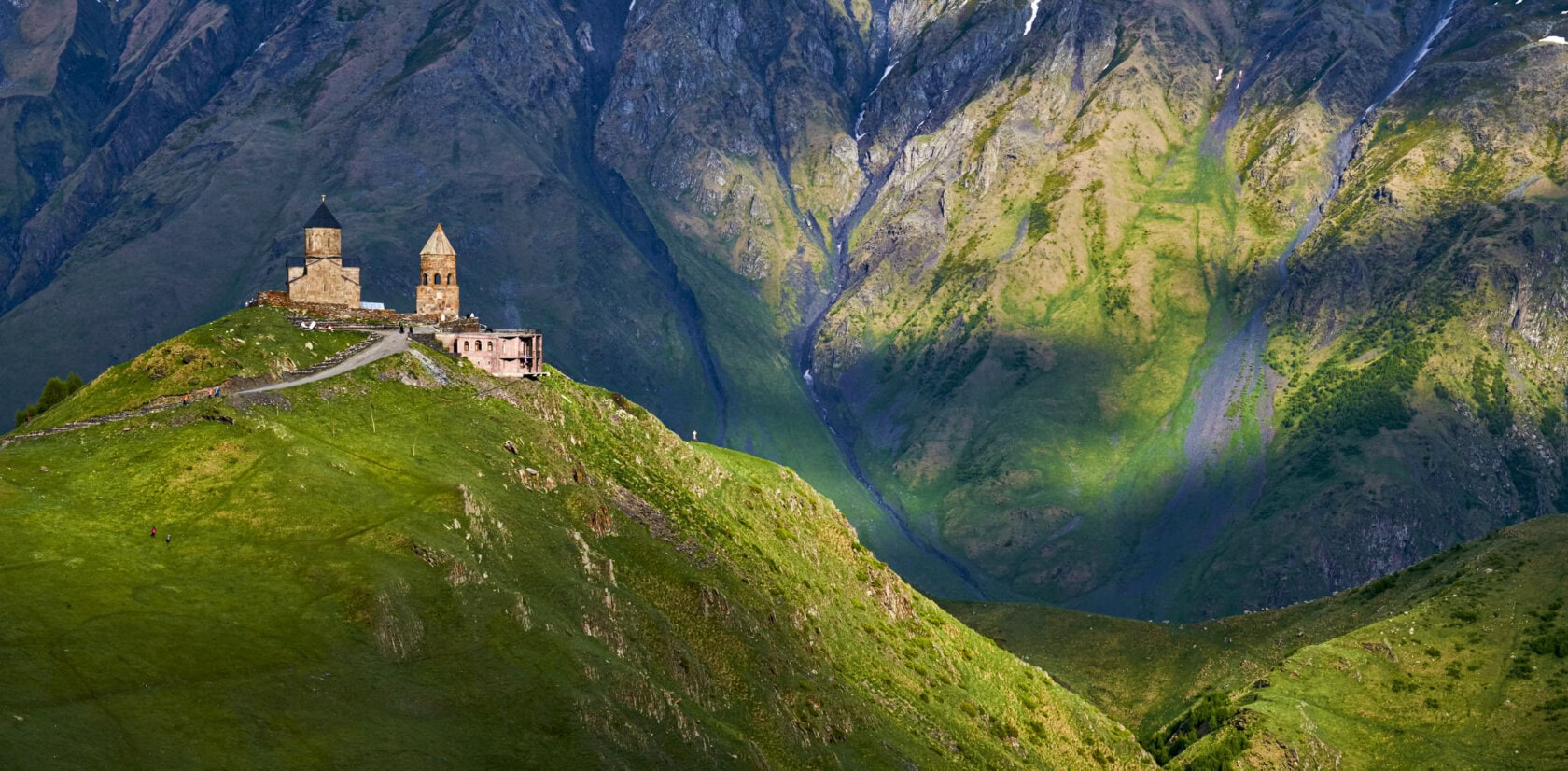 Gergeti Trinity Church perched on a green mountain hillside against a rugged range, a highlight to consider for the best time to visit Georgia.