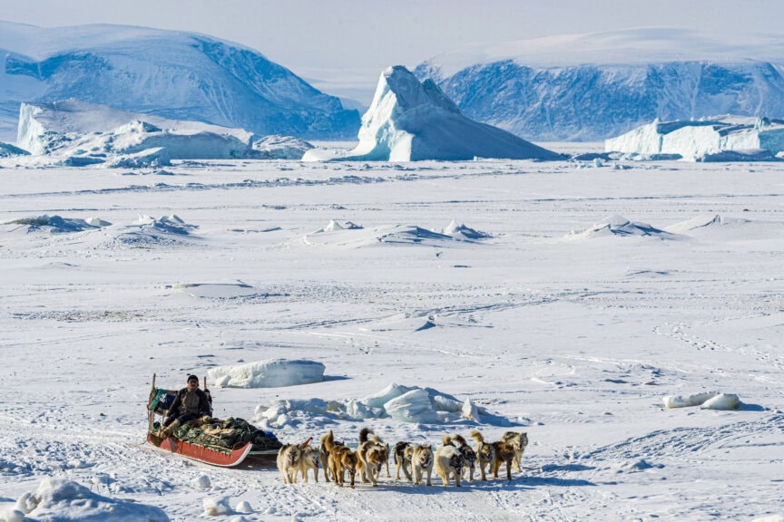 A person rides a sled pulled by dogs across snowy, icy landscapes—an adventure highlighting the best time to visit Greenland’s mountains and icebergs.