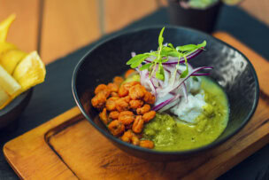 A bowl of ceviche with green sauce, toasted corn, and red onion, served with plantain chips, a staple of things to do in San José, Costa Rica.