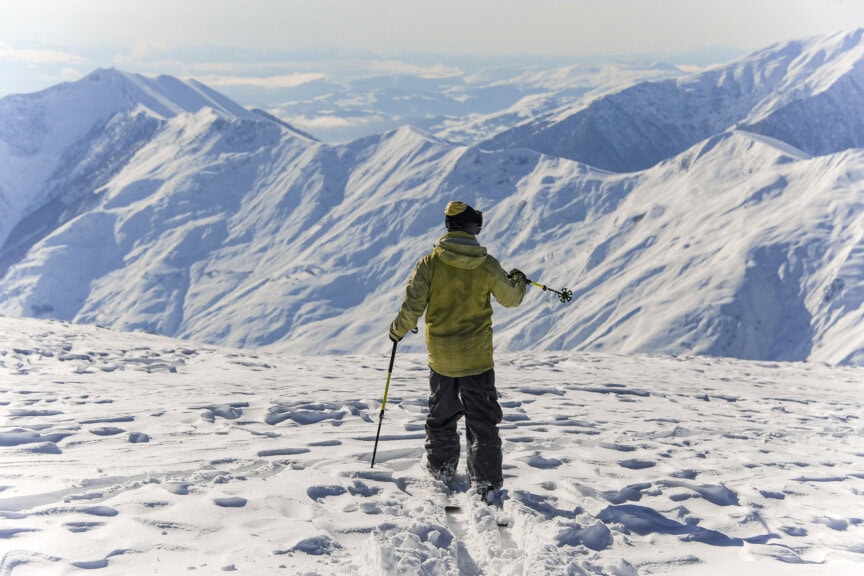 A skier standing on a snowy mountain ridge overlooking peaks, representing the best time to visit Georgia for winter sports.